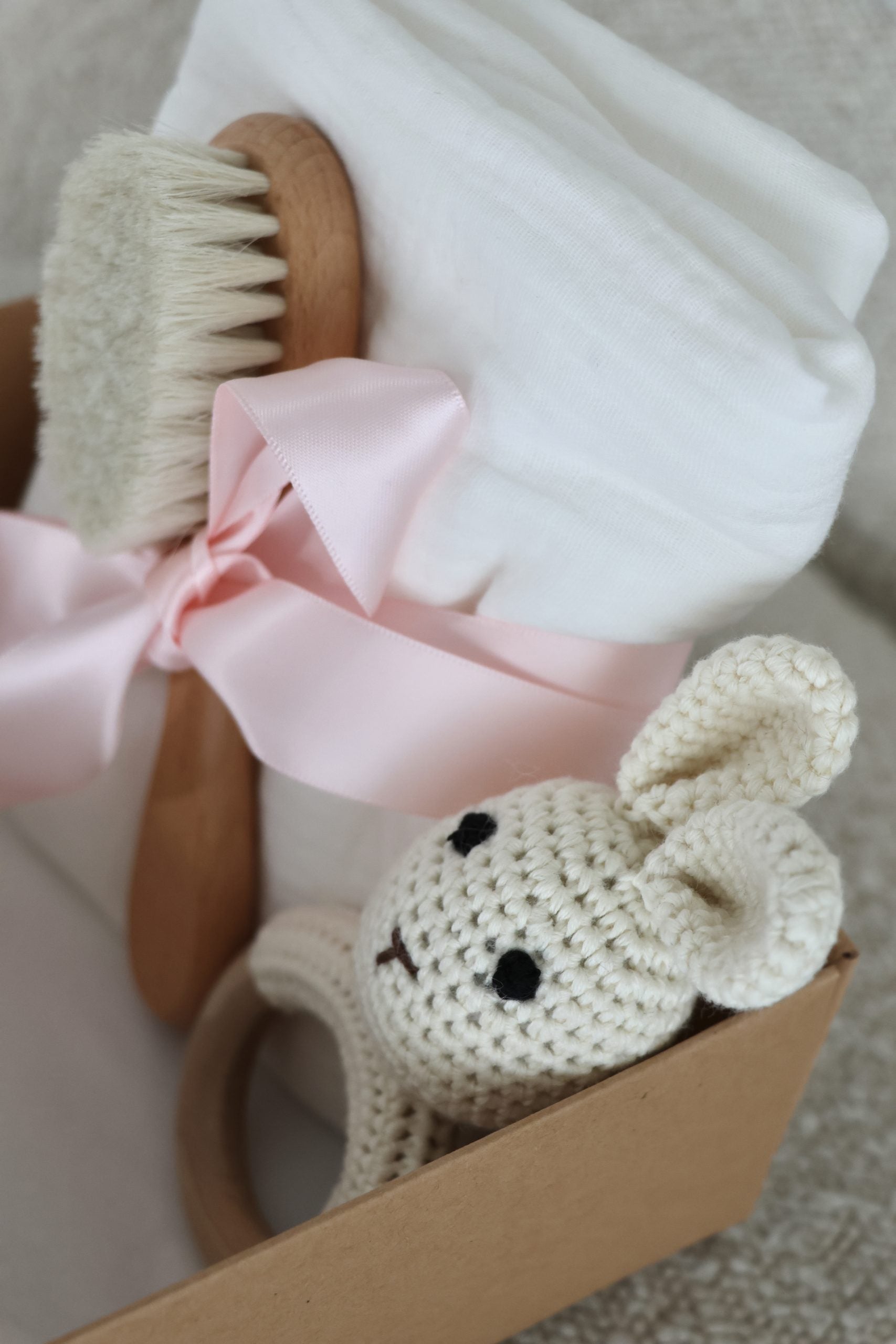 Coffret cadeau naissance pour bébé en bois et coton sur fond en bois, avec hochet lapin en crochet, lange tetra blanc et brosse à cheveux douce pour bébé.