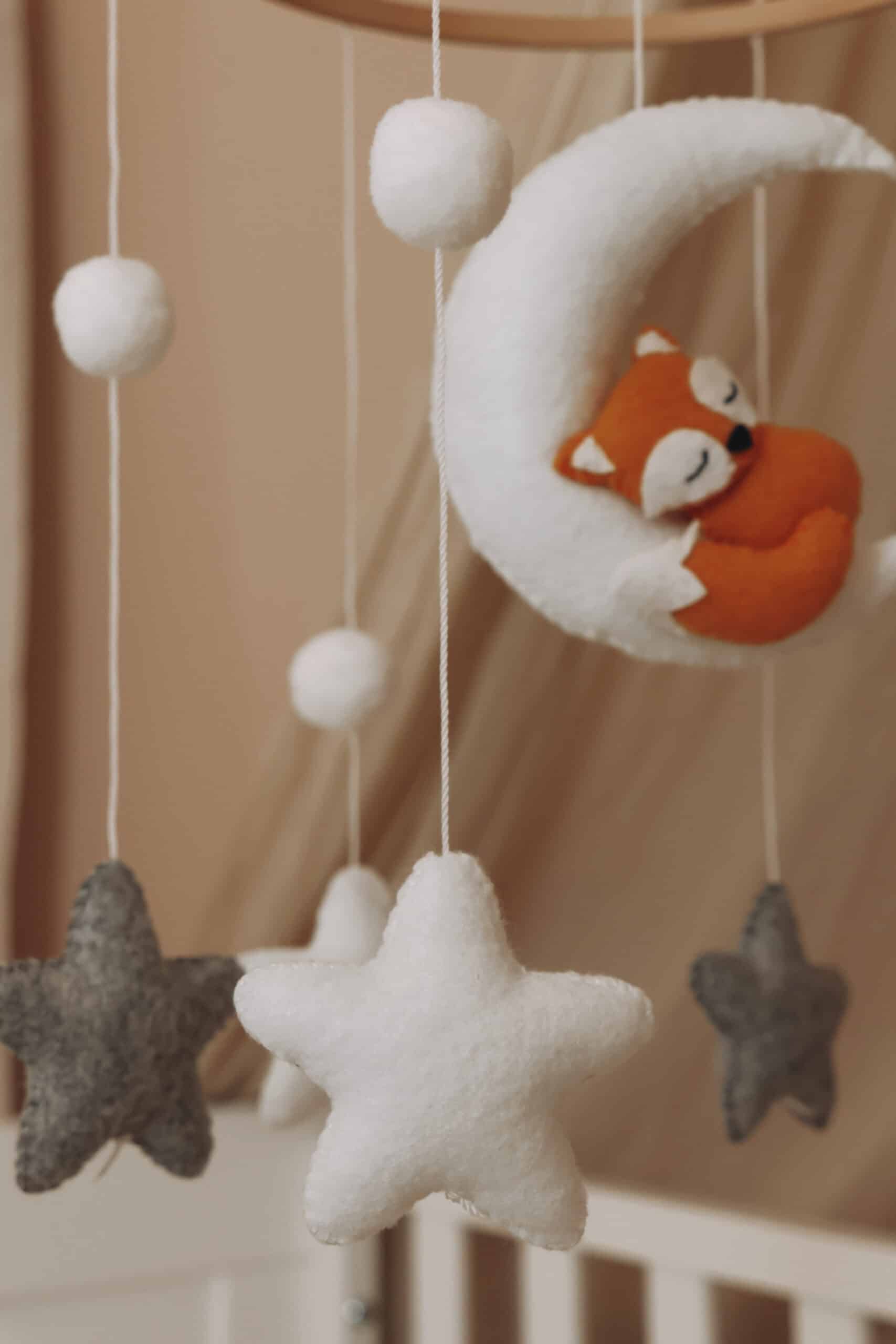 Mobile de lit pour bébé en bois avec un renard orange endormi sur un croissant de lune blanc, entouré d'étoiles et de boules en feutrine grises et blanches.