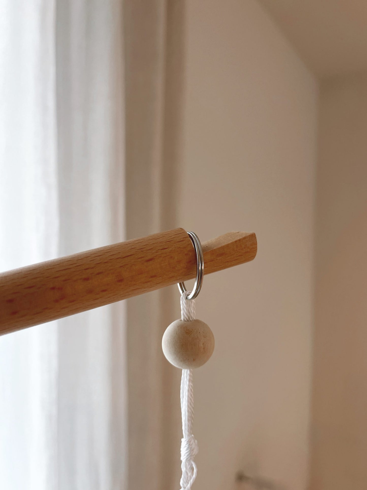 Vue de près du bout du bras de support. L'anneau du mobile se glisse dans une encoche. Potence ou bras de support universel en bois clair lisse, conçu pour suspendre un mobile au-dessus d'un lit pour bébé.