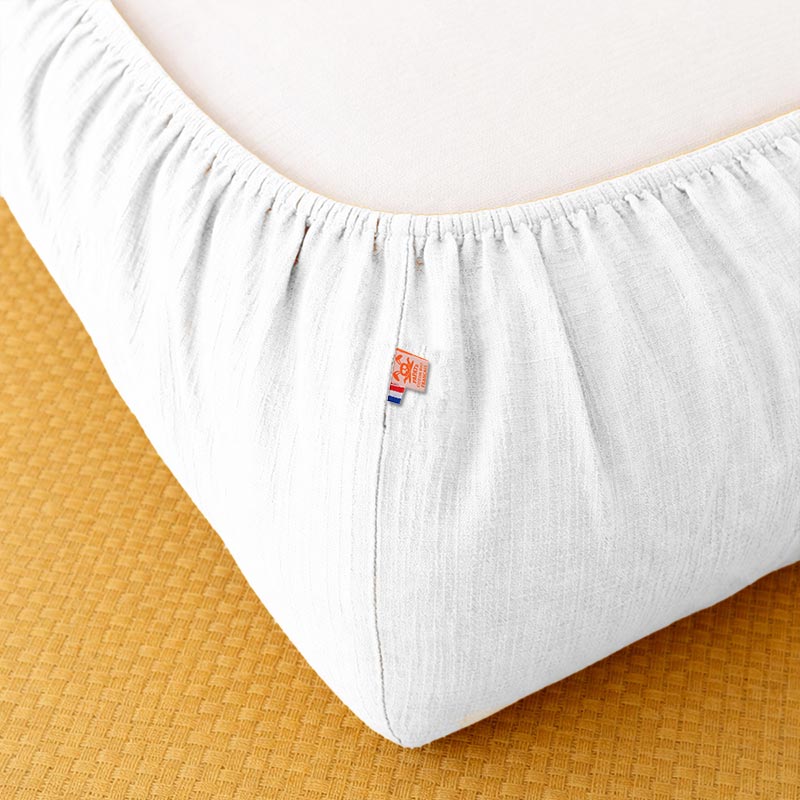 Drap housse pour lit de bébé en double gaze de coton biologique blanc, posé à plat et révélant sa texture gaufrée et douce. 60x120