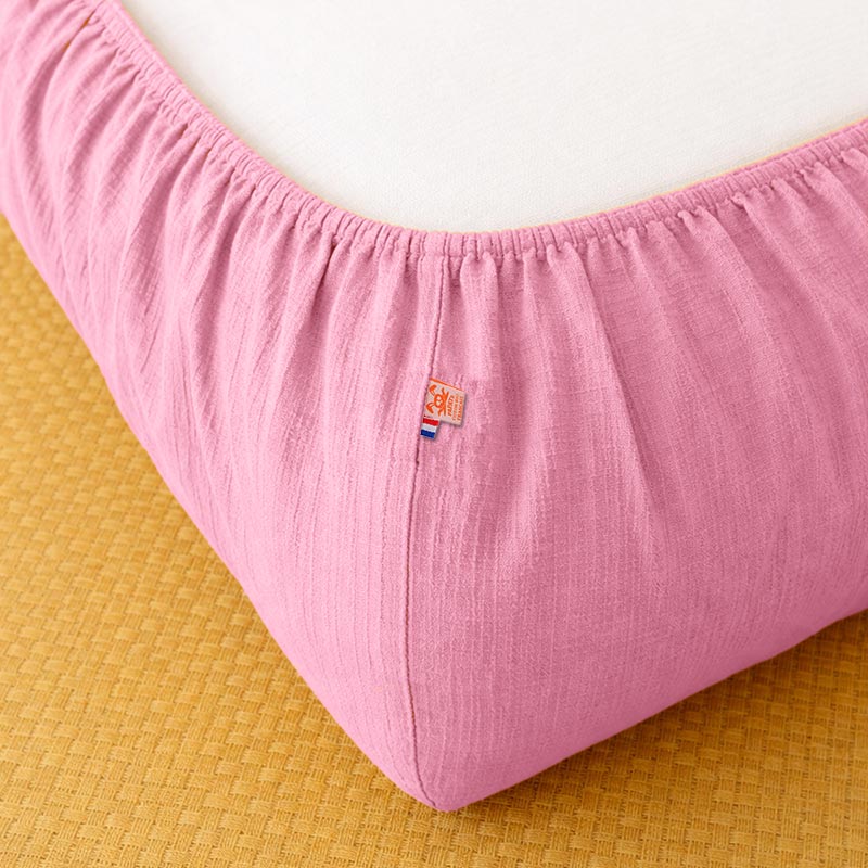 Drap housse pour lit de bébé en double gaze de coton biologique rose, posé à plat et révélant sa texture gaufrée et douce. 60x120