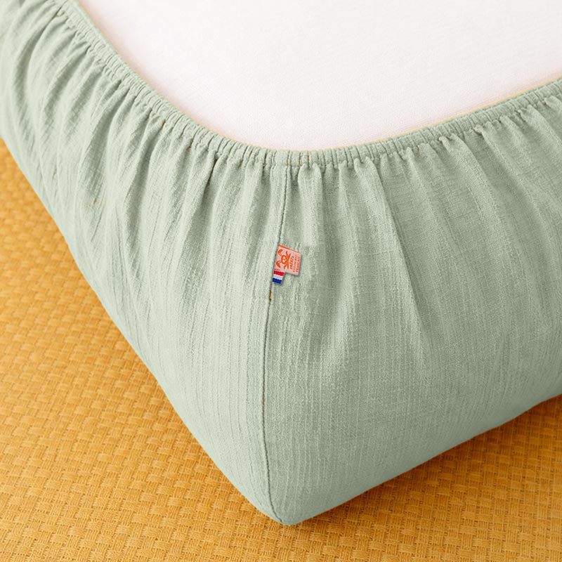 Drap housse pour lit de bébé en double gaze de coton biologique vert, posé à plat et révélant sa texture gaufrée et douce. 60x120