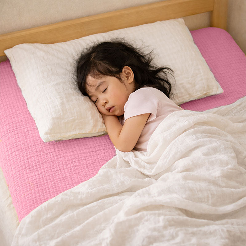 Drap housse pour lit de bébé en double gaze de coton biologique rose, posé à plat et révélant sa texture gaufrée et douce. 60x120