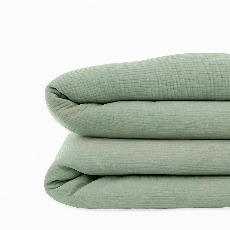 Housse de couette pour lit d'enfant en coton biologique de couleur vert sauge, pliée de manière élégante.