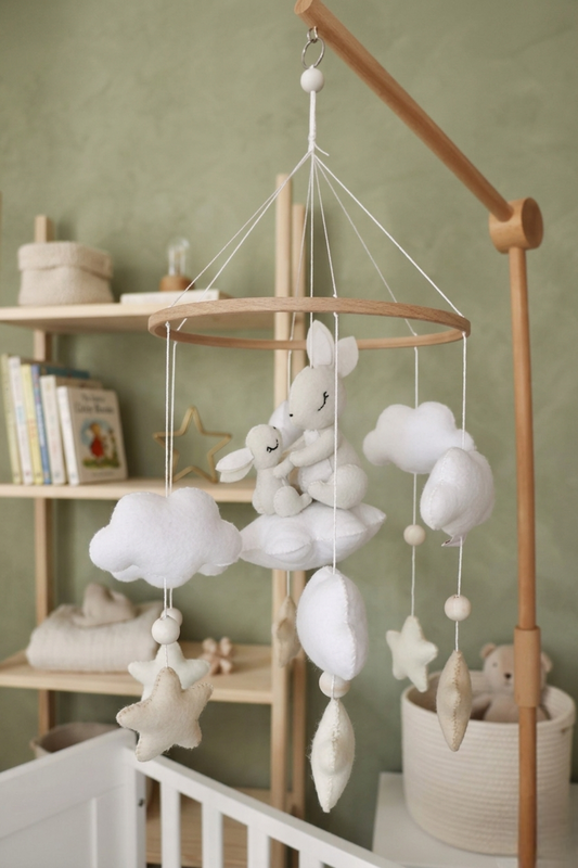 Mobile de berceau en bois pour bébé avec des peluches en feutrine blanche représentant une maman lapin et son petit assis sur un nuage, entourés d'étoiles beige et de nuages blancs.